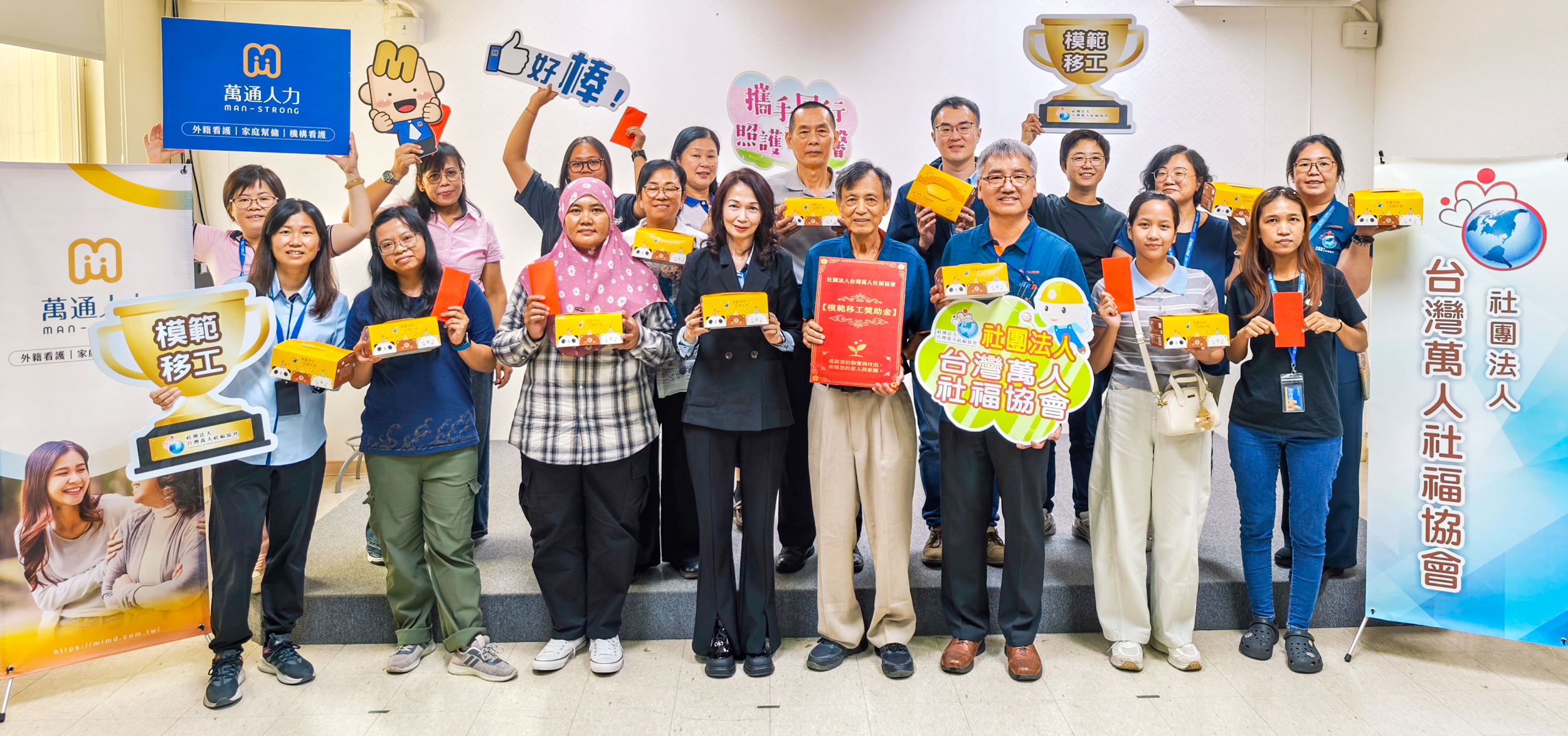 全體與會貴賓、獲獎移工及家屬開心合影，手持展翼烘焙庇護工場公益餐盒，共同見證感謝與公益同行的溫暖時刻。